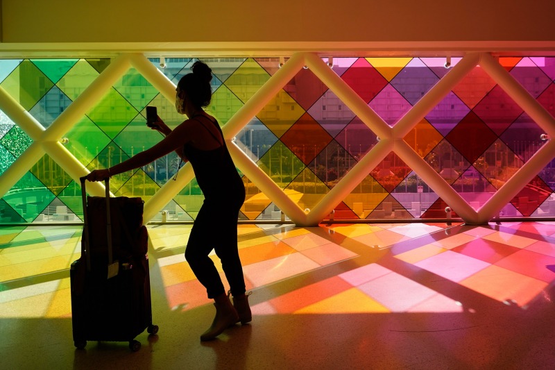 A traveller takes photos of windows titled "Harmonic Convergence," by artist Christopher Janney, Friday, May 28, 2021, at Miami International Airport in Miami. The Greater Miami Convention and Visitors Bureau is anticipating hotel occupancy levels to surge above pre-pandemic levels. (AP Photo/Wilfredo Lee)