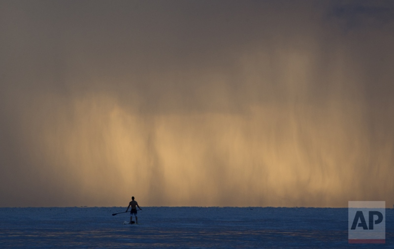 Pablo Dona, of Miami pauses while paddleboarding as sheets of rain fall in front of him, Tuesday, Sept. 22, 2015, off the shores of Bal Harbour, Fla. (AP Photo/Wilfredo Lee)