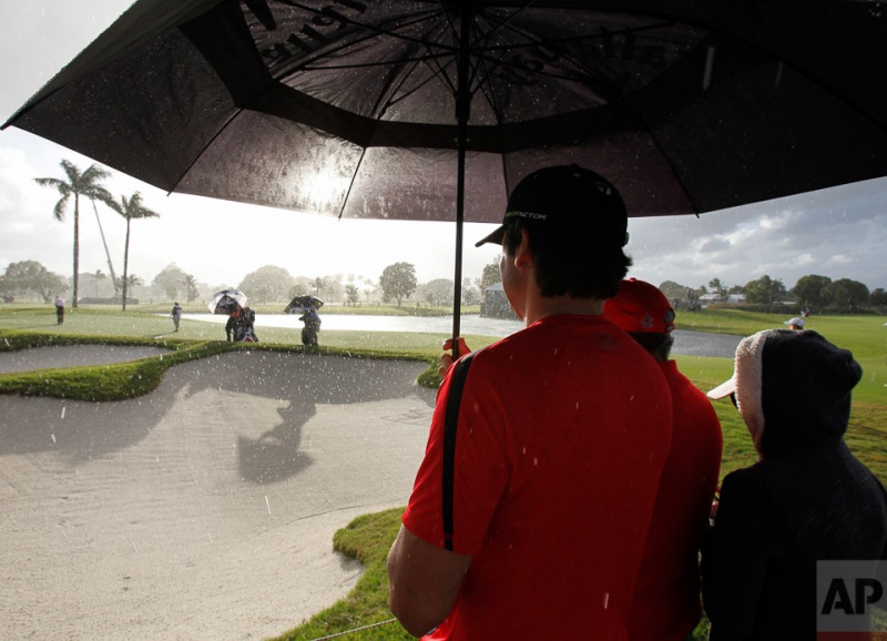 Fans watch play on the eighth hole during a rain shower during the first round of the Cadillac Championship golf tournament, Thursday, March 8, 2012, in Doral, Fla. (AP Photo/Wilfredo Lee)